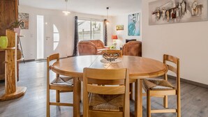 Un coin repas comprenant une table ronde en bois, six chaises en bois et un lustre.