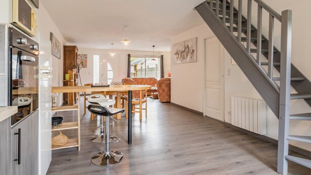 Une cuisine moderne avec des meubles en bois, un coin repas avec une table et des chaises en bois, et un escalier avec des rampes en métal.