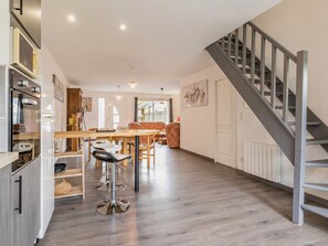 A modern kitchen with wooden cabinets, a dining area with a wooden table and chairs, and a staircase with metal railings. - Quiet cottage in nature near Nantes (Héric)