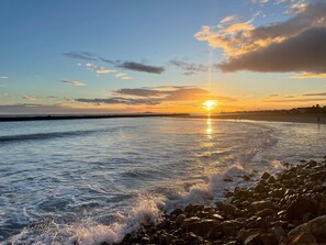A beach scene with the sun setting over the horizon, waves crashing onto the shore, and a rocky coastline. - Studio with air conditioning and parking, close to the beach (Sète)