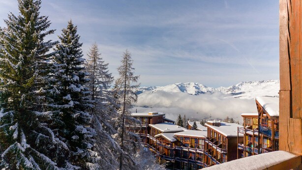 A snow-covered lodge with multiple buildings, a wooden balcony, and a view of snow-capped mountains in the background. - Ski-in duplex for 6 in Arc 1800, southeast balcony (Les Arcs 1800)