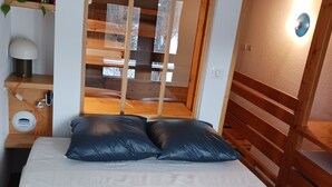 A bedroom with a bed, two pillows, a bedside lamp, a power outlet, and a window with a view of a wooden structure outside. - Ski-in duplex for 6 in Arc 1800, southeast balcony (Les Arcs 1800)