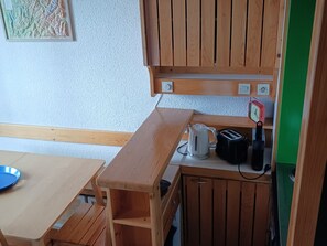 A compact kitchen with wooden cabinets, a countertop, a kettle, a toaster, and a clock.