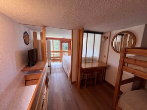 A compact room with a bunk bed, a desk, a television, and a window providing a view of the outdoors.