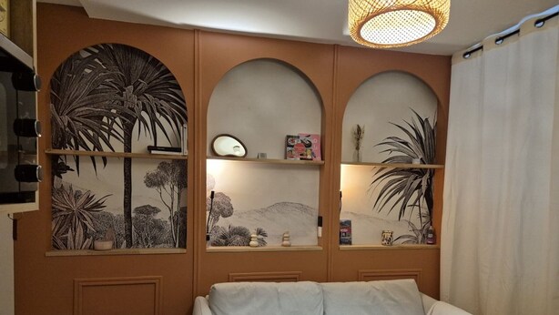 A living room with a sofa, a wall with three shelves displaying decorative items, and a hanging light fixture. - Cozy 17m² studio, near cable car, 2/4 pers, parking (Cauterets)