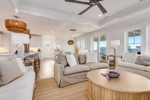 A spacious living area with a high ceiling, a ceiling fan, and large windows offering a view of the city. - Brand NEW! 5 Bedroom home off South Bald Head (Bald Head Island)