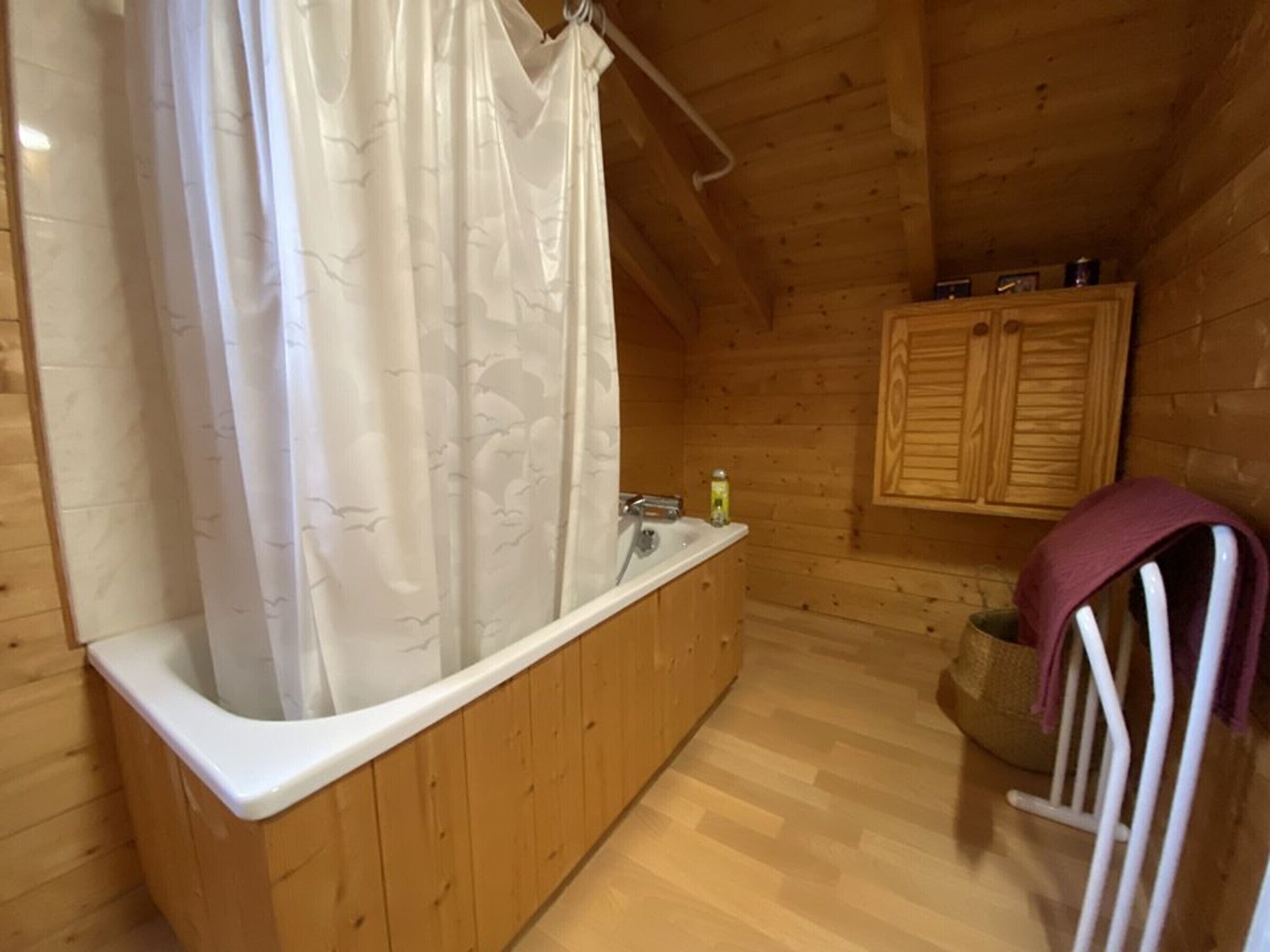 Ein Badezimmer einer Holzhütte mit Badewanne, einer Duschvorhangs und Holzschränken sowie einem Handtuchhalter.
