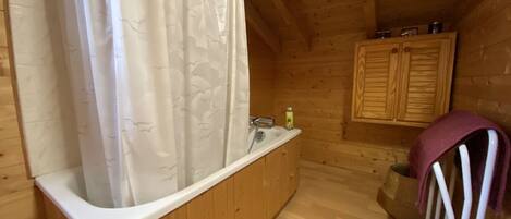 Ein Badezimmer einer Holzhütte mit Badewanne, einer Duschvorhangs und Holzschränken sowie einem Handtuchhalter.