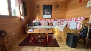 Ein gemütliches Blockhaus-Interieur mit Holzvertäfelung, einer Couch mit gemusterten Kissen, einem kleinen Tisch und einem Teppich.