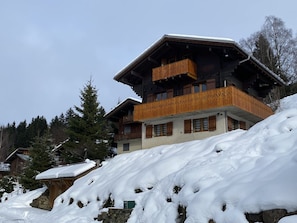 Ein mehrstöckiges Chalet mit Holzbalkonen, umgeben von verschneiter Landschaft und Bäumen.