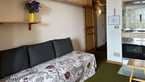 Un espace de vie compact comprenant un canap é, des meubles en bois, un petit coin cuisine avec un four et une moquette verte.