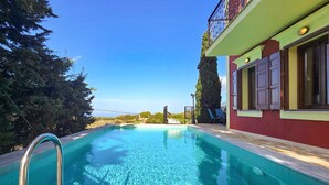 Ein klares, blaues Schwimmbecken mit einer Metallleiter, umgeben von Bäumen und einem Gebäude mit Balkon.