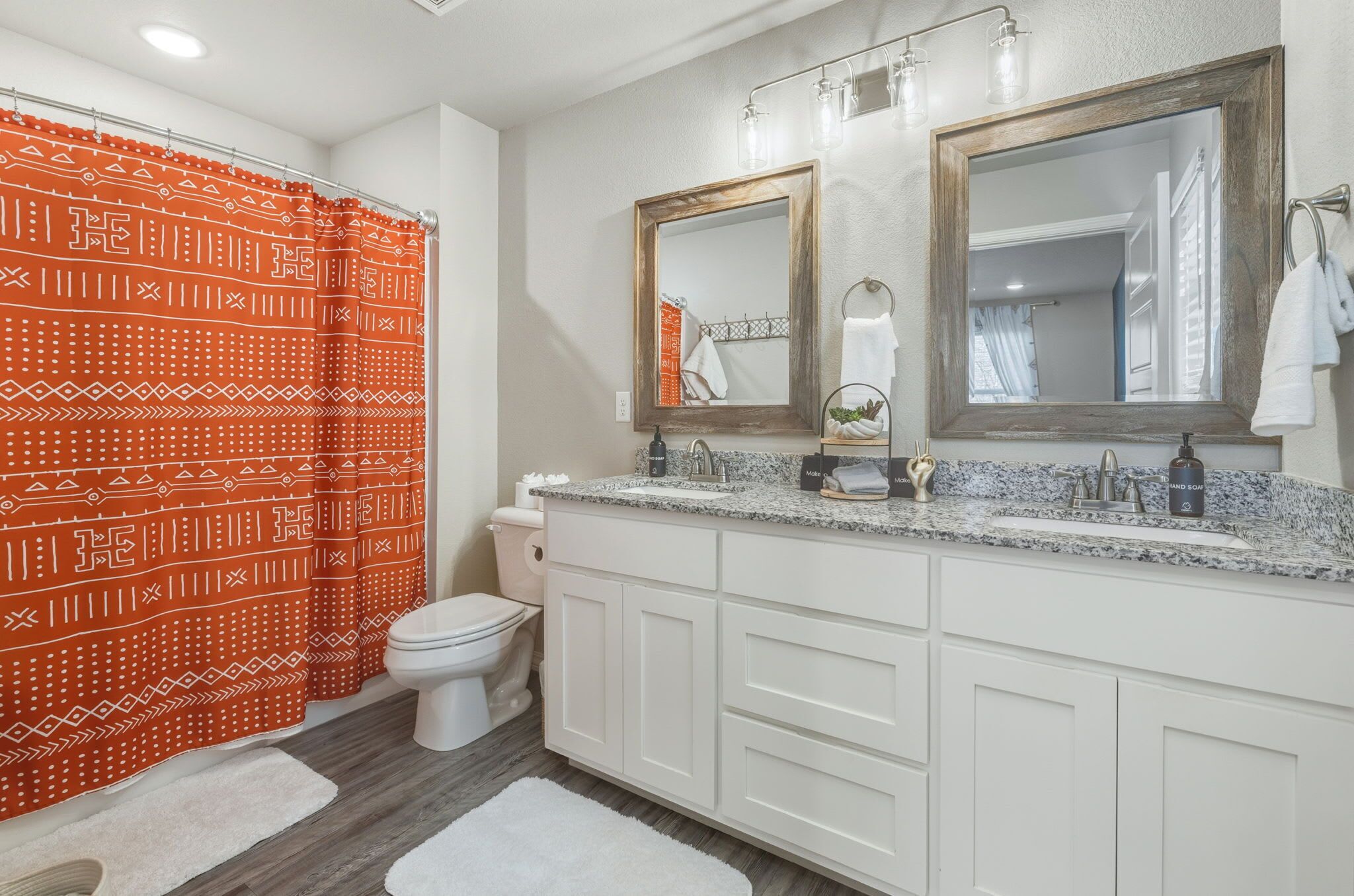 A bathroom with a white toilet, double sinks, a large mirror, and a shower curtain with a geometric pattern.