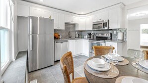 A modern kitchen with white cabinets, stainless steel appliances, and a dining area with wicker chairs and a table set for four.