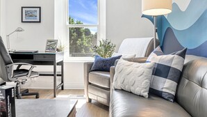 A modern living room with a leather sofa, a desk, and a large window with a view of greenery.