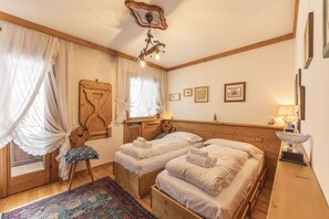 A cozy room with two wooden beds, a wooden chair, a patterned rug, and a ceiling light fixture. - Casa La Marignana, welcoming and comfortable (Cortina d´Ampezzo)
