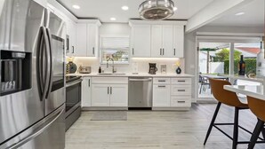 Una cocina moderna con gabinetes blancos, electrodomésticos de acero inoxidable y un comedor con un taburete de bar.