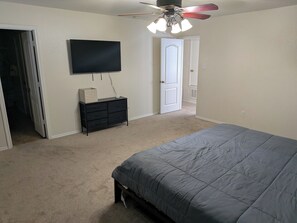 A bedroom with a bed, a dresser, a television, and a ceiling fan.