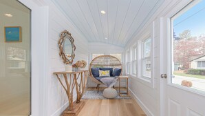 A hallway with a wooden floor, a wicker chair with cushions, a mirror, and a small table with a vase. - Coastal Retreat at Lemon Tree Cottage (Marion)