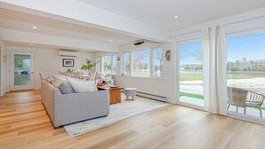 A spacious living room with a grey sofa, a wooden coffee table, and a view of a green landscape through large windows. - Coastal Retreat at Lemon Tree Cottage (Marion)