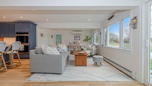 A spacious living area with a grey sofa, wooden coffee table, and wicker chairs. A kitchen with dark cabinets and a built-in oven is visible in the background. - Coastal Retreat at Lemon Tree Cottage (Marion)