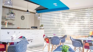A modern dining area with a white curved counter, blue ceiling accents, and a large window with horizontal blinds. - Glory Sanctuary Retreat (Citluk)