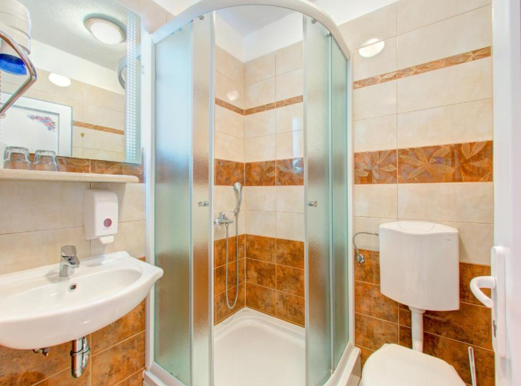 A bathroom with a glass-enclosed shower, a sink, a toilet, and a hand dryer.