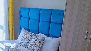 A bed with a blue headboard, white pillows, and a patterned pillow. - Affordable Studio Apartment Near JKIA, Fedha Embakasi. (Nairobi)