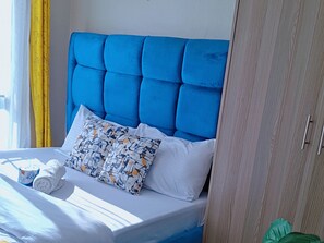Een bed met een blauw hoofdeinde, witte kussens en een gestreept kussen.