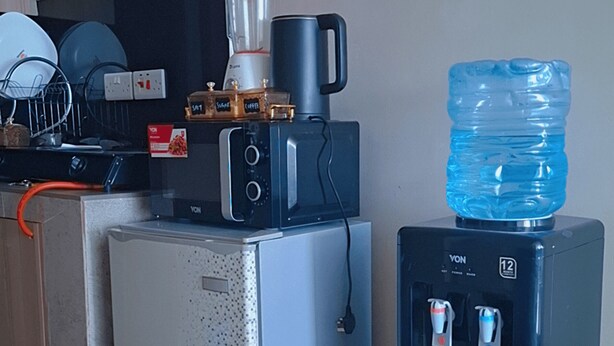 A kitchenette with a refrigerator, a coffee maker, a blender, and a water dispenser. - Affordable Studio Apartment Near JKIA, Fedha Embakasi. (Nairobi)