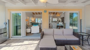 A spacious living area with a large wicker sofa, a glass door leading to a kitchen, and a ceiling fan. - 🏝️Private Pool | Canal Front | Beautiful Life on Madison🏝️ (Fort Myers Beach)