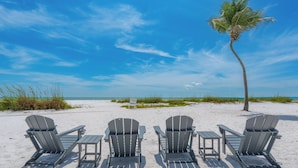A beach with four Adirondack chairs and a palm tree. - 🏝️Private Pool | Canal Front | Beautiful Life on Madison🏝️ (Fort Myers Beach)