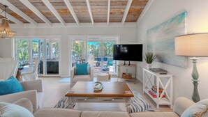 A modern living room with a wooden ceiling, a flat-screen TV, a painting, and a dining area with outdoor views. - 🏝️Private Pool | Canal Front | Beautiful Life on Madison🏝️ (Fort Myers Beach)