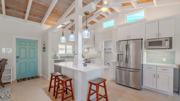 A spacious kitchen with white cabinetry, a large island with stools, stainless steel appliances, and a wooden ceiling with skylights. - 🏝️Private Pool | Canal Front | Beautiful Life on Madison🏝️ (Fort Myers Beach)