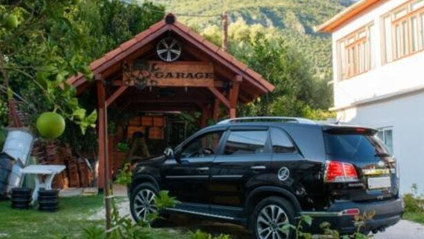 A black SUV parked in front of a building with a 'GARAGE' sign, surrounded by greenery and a mountainous backdrop. - Apartments Savić Near the Sea (Denovici)