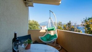 A balcony with a round table, a hanging chair, a bottle of wine, and a glass. - Apartments Savić Near the Sea (Denovici)