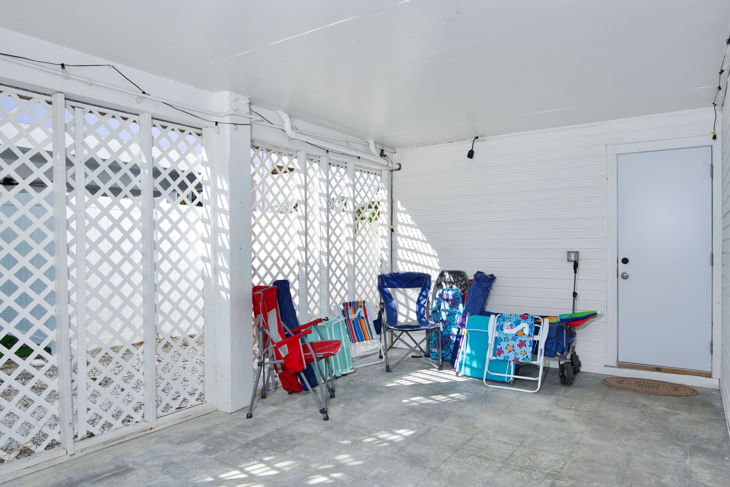 A covered patio area with white lattice panels, a door, and several folding chairs.