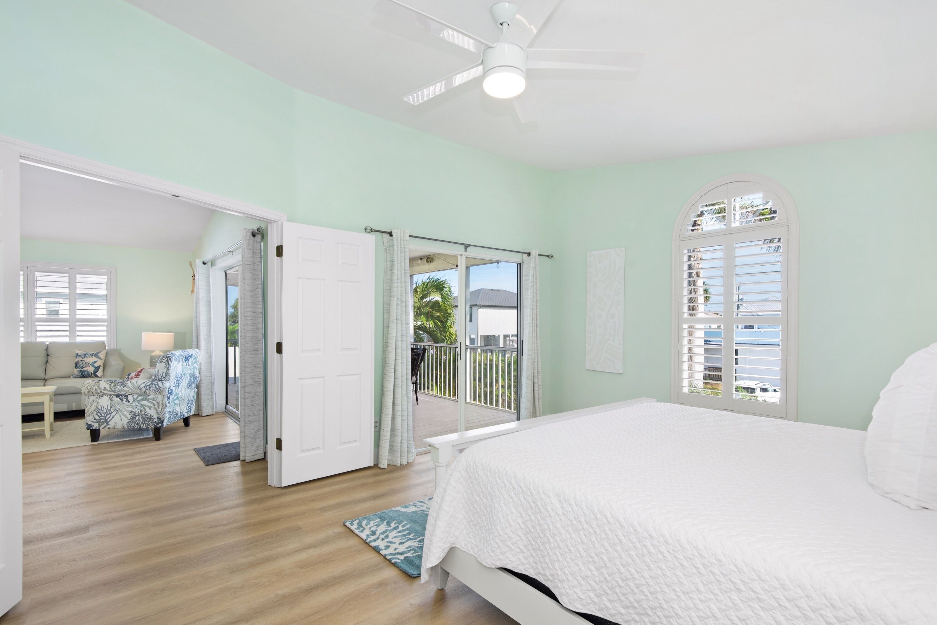 A bedroom with a bed, a ceiling fan, and a view of the outside balcony.