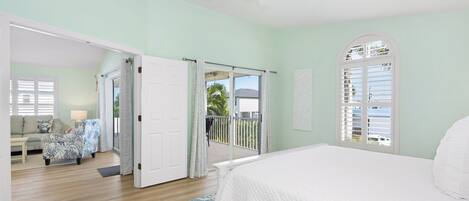 A bedroom with a bed, a ceiling fan, and a view of the outside balcony.