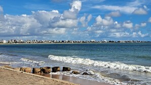Un paisaje urbano costero con una playa en primer plano, que presenta un litoral rocoso y olas.