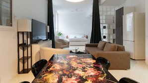 Ein modernes Wohnzimmer mit Esstisch, Sofa, Fernseher und Küchenzeile.