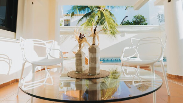 A round glass table with two white chairs, two glass bottles with dried flowers, and a woven placemat. - House with Private Pool - 3BR Cancun Downtown Zone (Cancún)