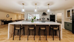 Une cuisine spacieuse dotée d’un grand îlot central, de trois luminaires suspendus et donnant sur la salle à manger.