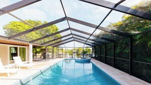 Une piscine intérieure dotée d’un toit en verre, entourée de chaises longues et offrant une vue sur la verdure.