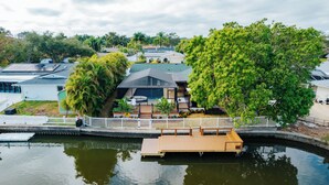 Une propriété située au bord de l’eau, dotée d’un quai, d’un espace extérieur couvert et d’une maison avec un toit en pente.
