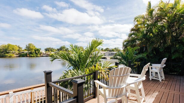 Une terrasse en bois avec des chaises blanches donnant sur un lac, le tout entouré d’une végétation luxuriante.