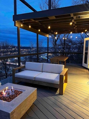An outdoor deck with a fire pit, a sofa, and string lights. - Luxury Mountainside with Spectacular Views (Pittsburgh)