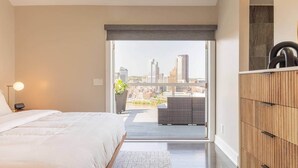 Une chambre à coucher avec un lit, une lampe de chevet et une vue sur le paysage urbain, visible à travers une grande fenêtre.