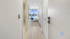 A hotel corridor with a bed in the distance, a city view through large windows, and a 'Stay Sol' logo on the wall. - Upper Studio w/ Private Balcony + Fitness Center (Hallandale Beach)