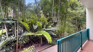 A balcony with a view of dense tropical foliage, a tiled floor, and a teal railing. - Magnetic Reef 5 (Arcadia)